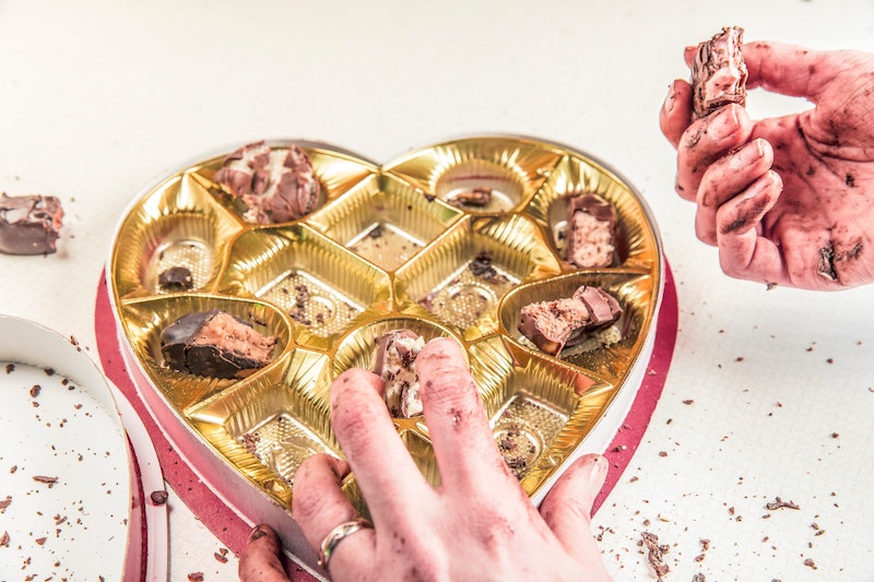 Mains d'une femme ayant mangé tous les chocolats d'une boîte en forme de coeur.  