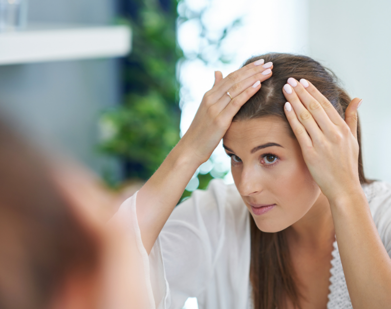 Jeune femme brune qui se regarde dans le miroir pour observer son psoriasis au cuir chevelu